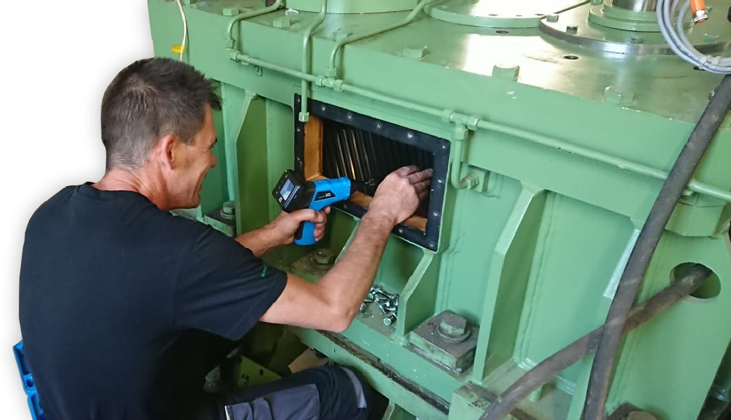 Ein Monteur der Firma KACHELMANN GETRIEBE GmbH repariert ein grünes Getriebe. Er hockt links neben dem Getriebe und lacht. Einige Schrauben liegen auf dem grünen Getriebe. KACHELMANN GETRIEBE GmbH